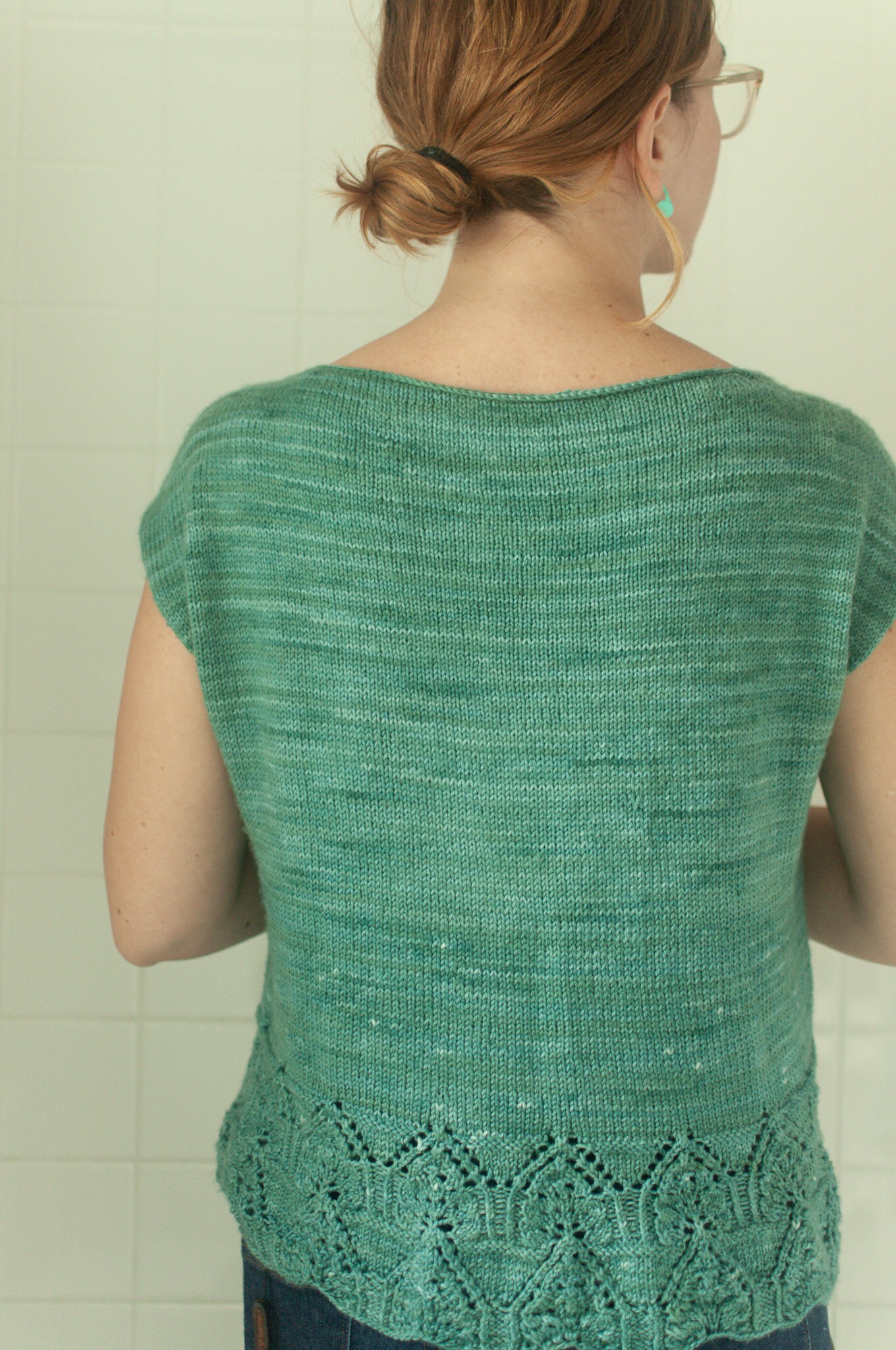 Woman models back of knitted crop top with lace edge